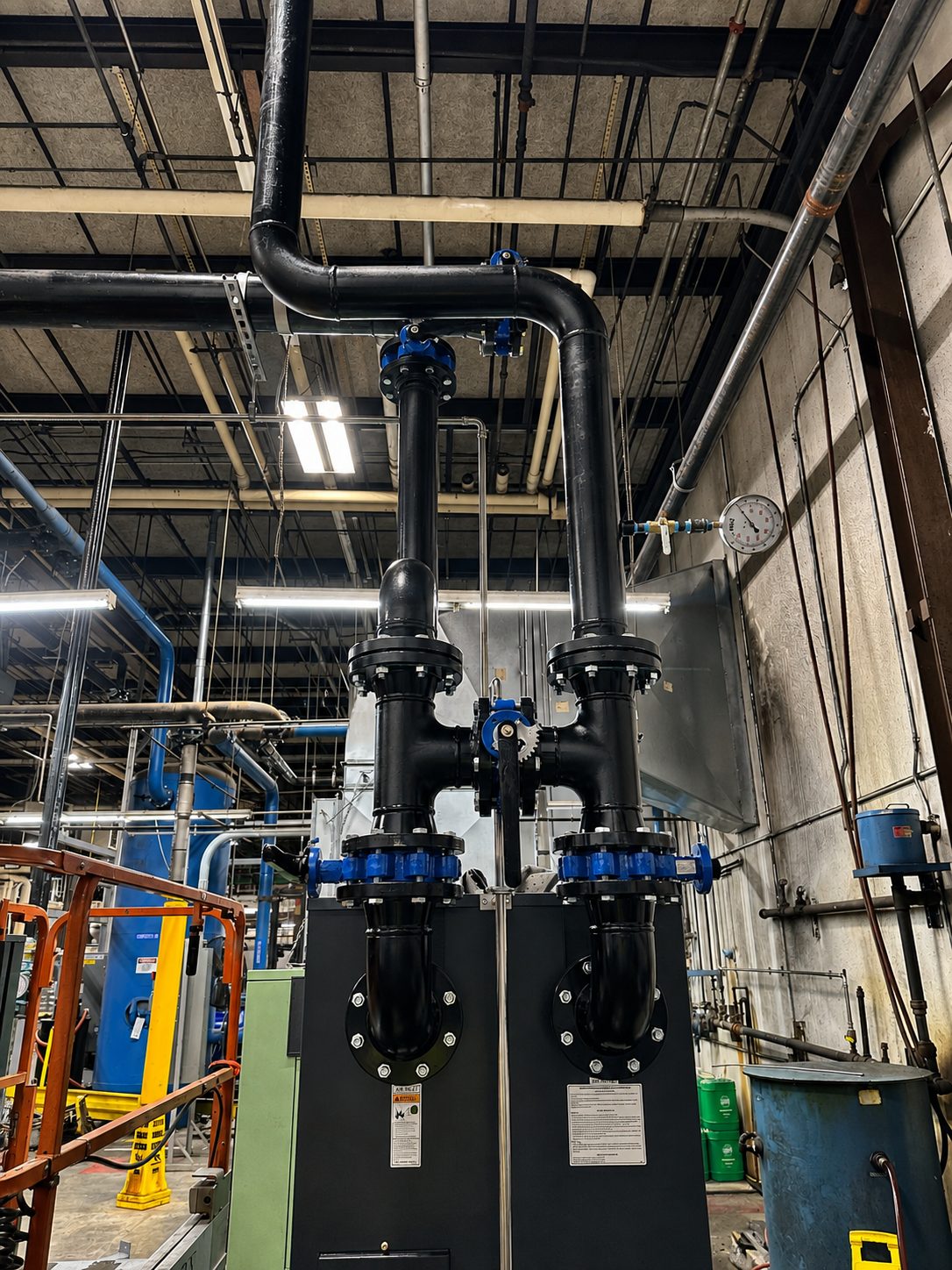 Black process piping and valve assembly installed against a plant wall